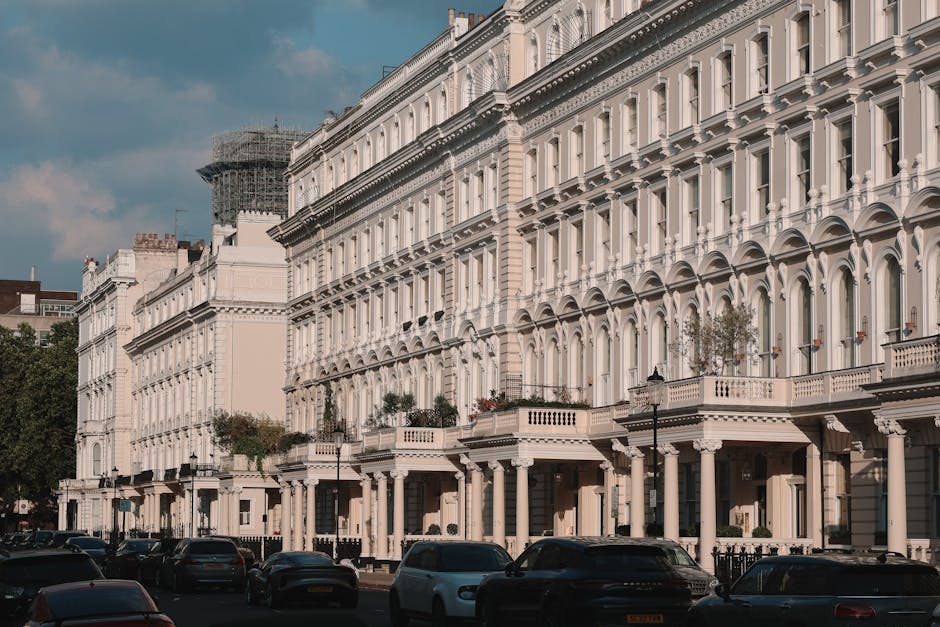 A row of elegant, white Victorian-style terraced townhouses with ornate architectural details, including columns, balustrades, and decorative window frames, situated along a street in South Norwood. T